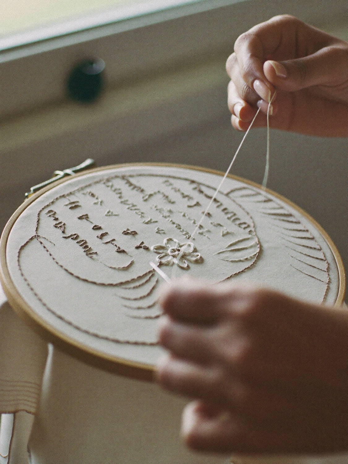 Hands working gold thread embroidery on cream silk