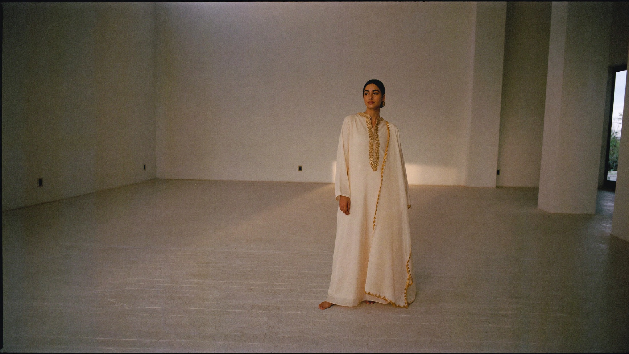 A woman in an ivory chanderi silk kurti standing in a bare sunlit room